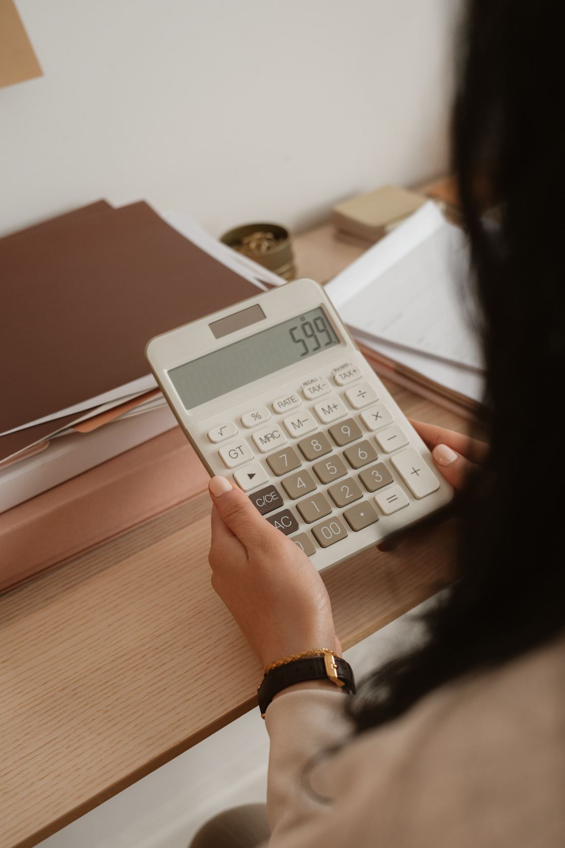 A woman at a desk holding a calculator, papers and folders stacked beside her.
