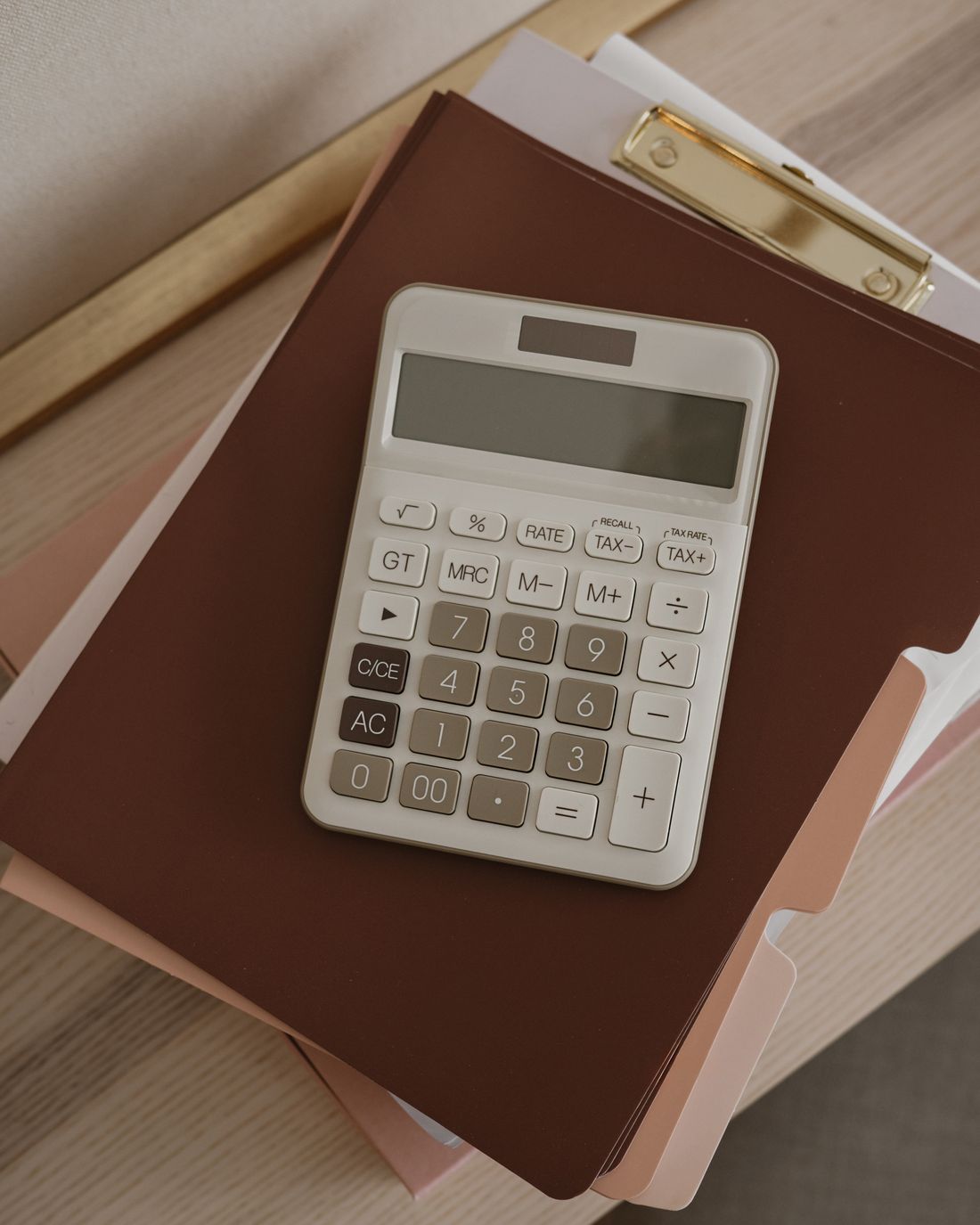 A calculator resting on a stack of folders and a clipboard on a desk.